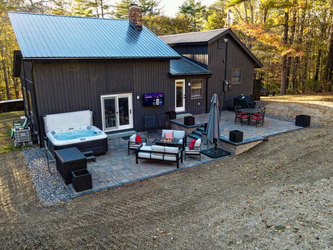 Modern black house exterior with patio, hot tub, and outdoor seating in a serene setting.