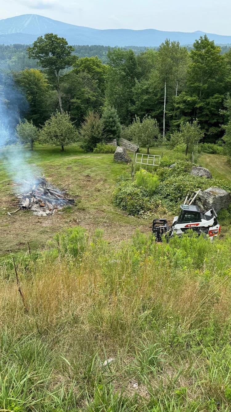Clearing land with a vehicle near a controlled burn and forested area.