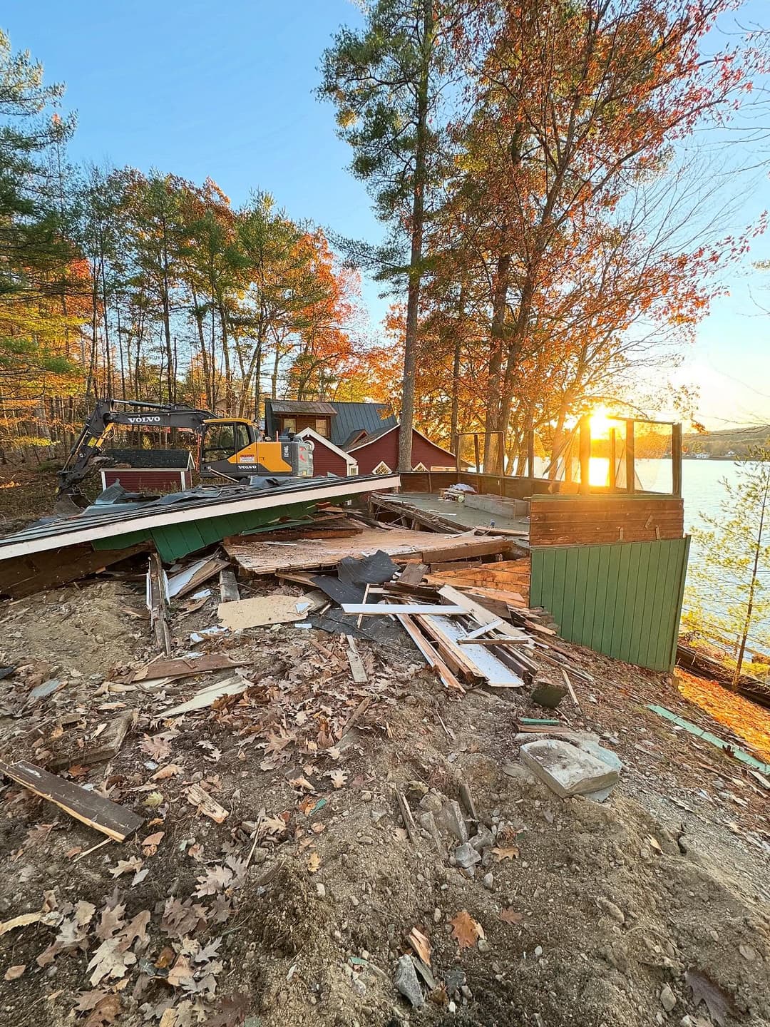 Damaged cabin by the lake at sunset, debris scattered amid autumn foliage.