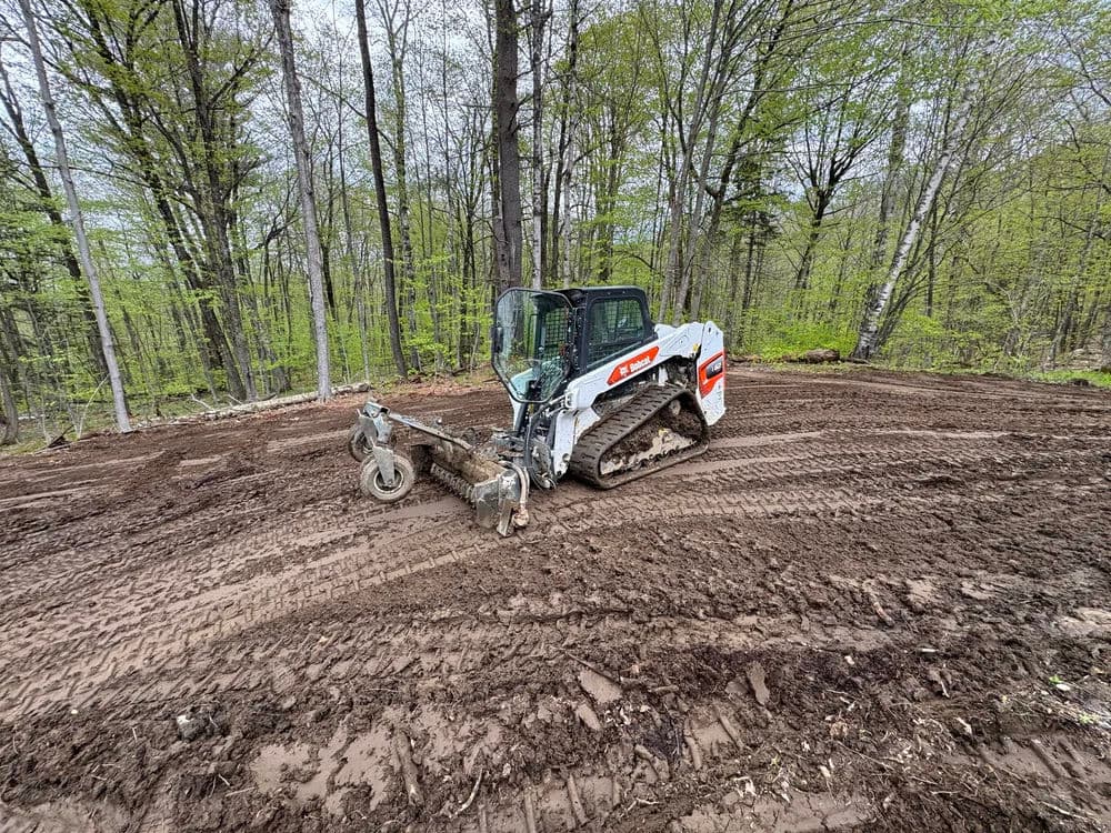 Excavator on muddy terrain in a forested area with fresh tire tracks.