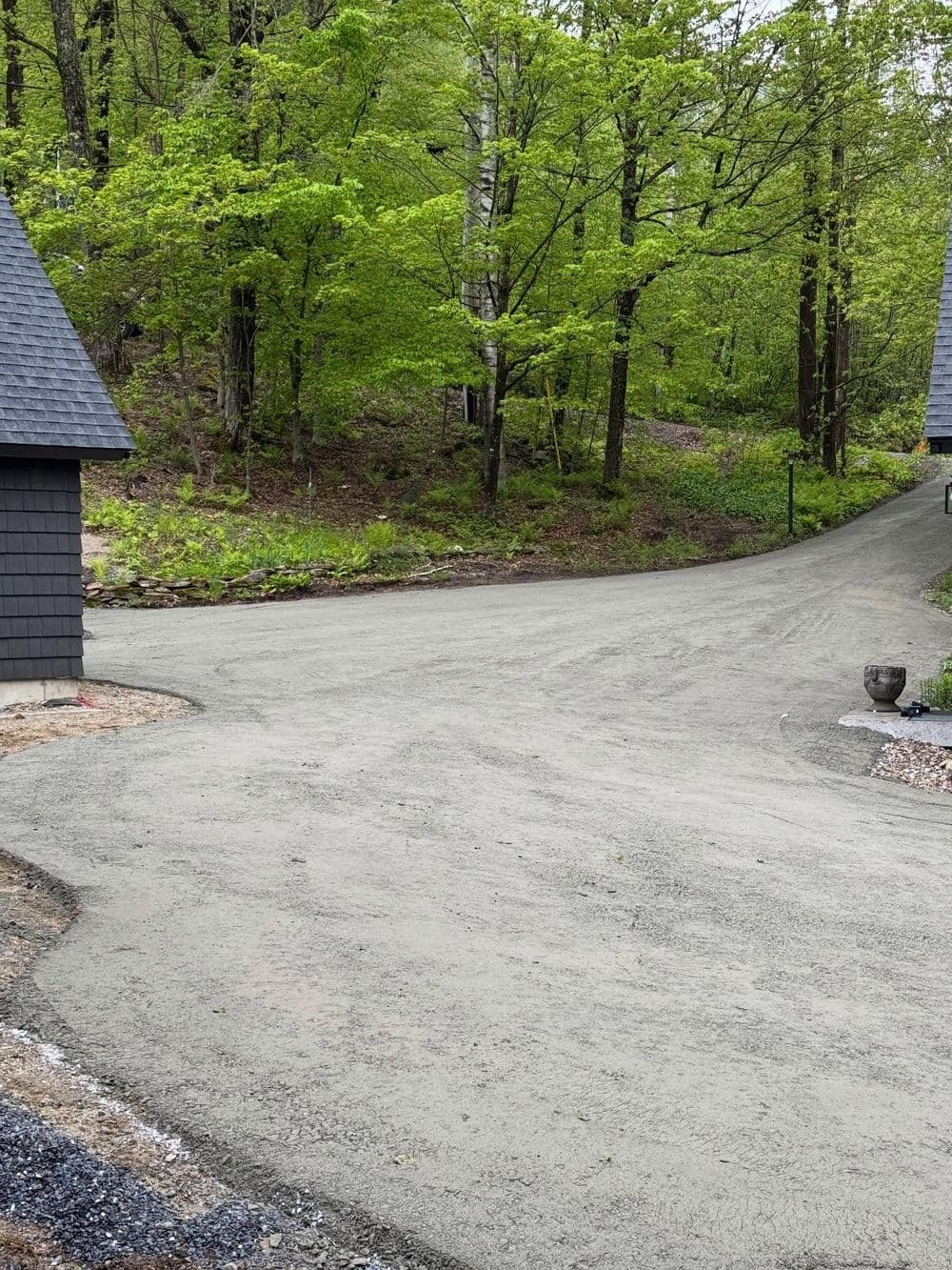 Freshly paved gravel driveway winding through lush green forest scenery.